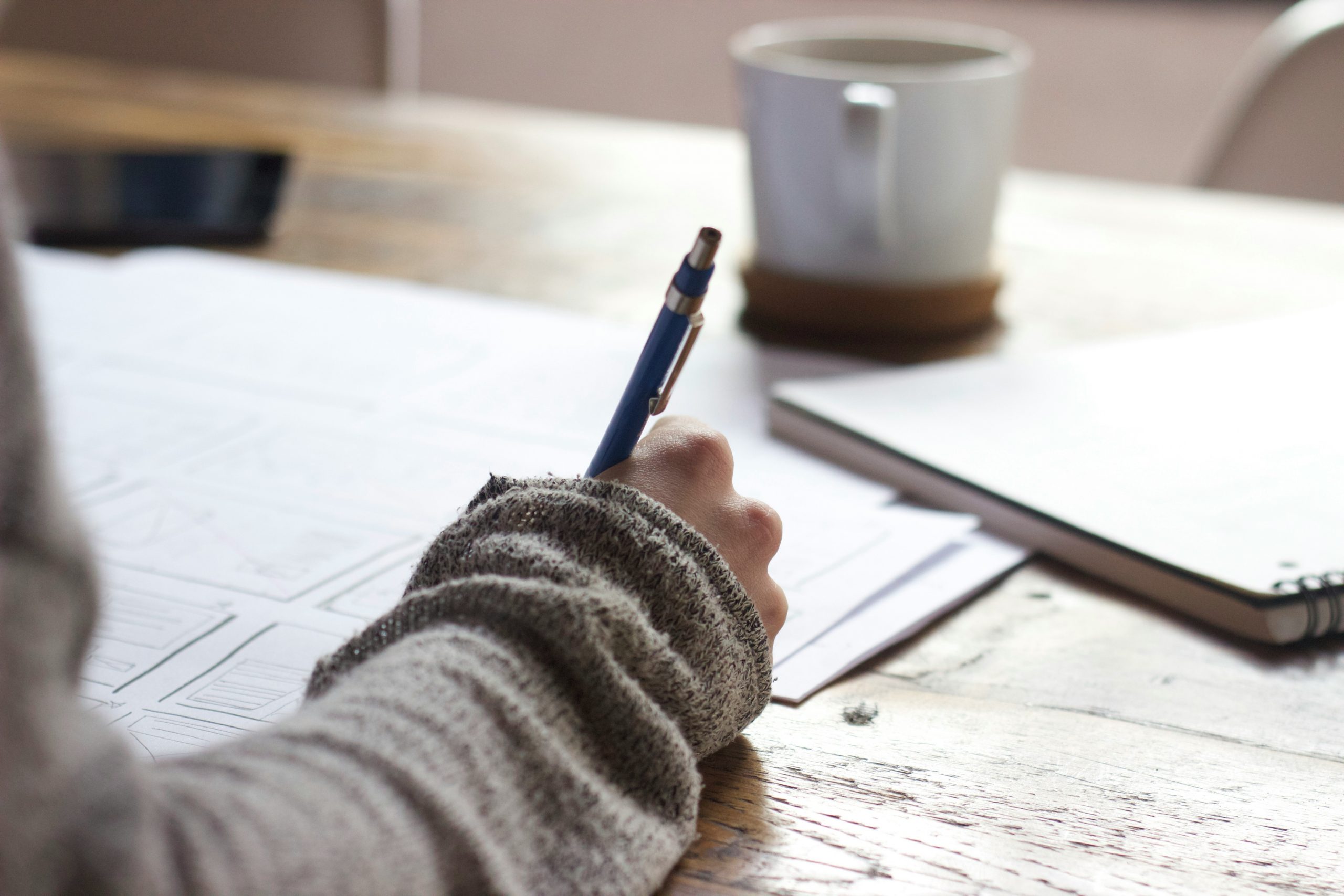 someone taking notes by hand with a cup of coffee